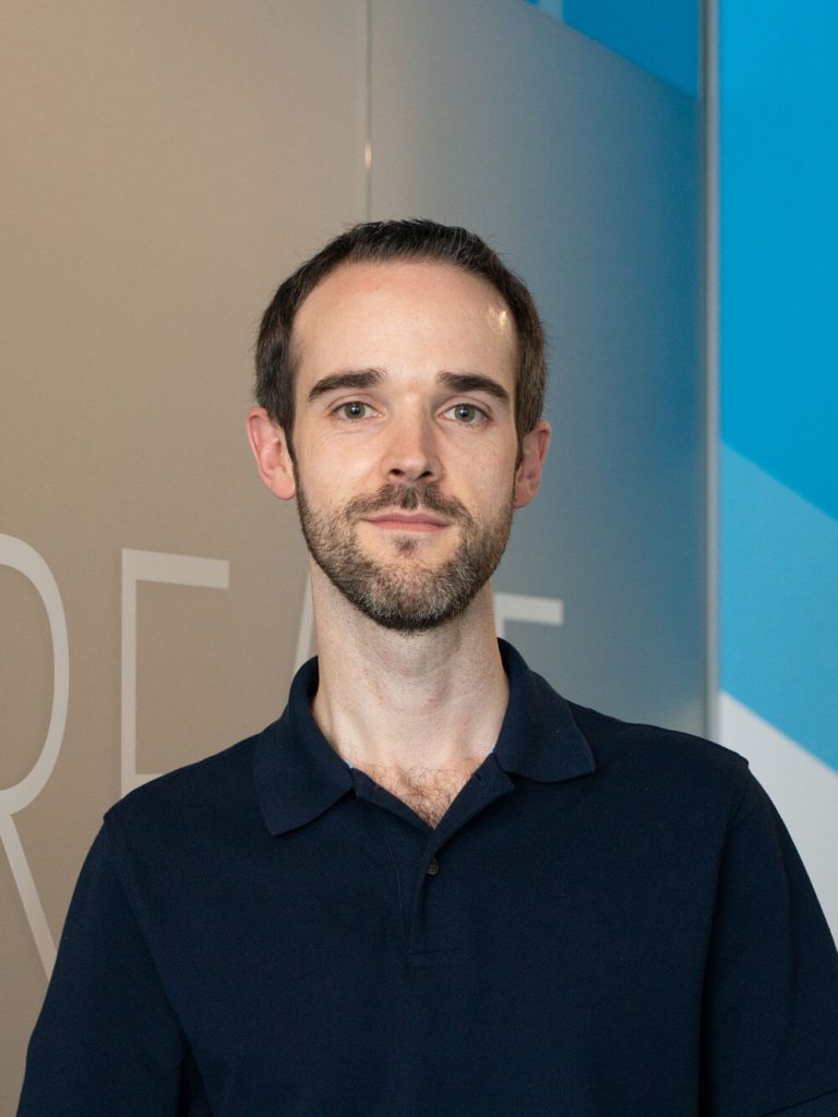 Portrait of a Resolute Cyber team member Paul standing in front of a modern office backdrop.